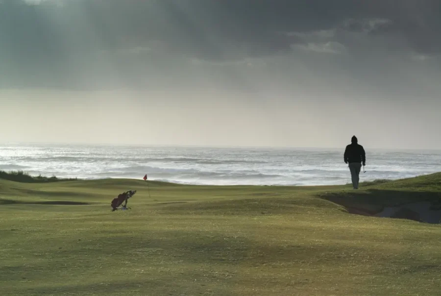 silhouette of man walking on golf course with sea in the background
