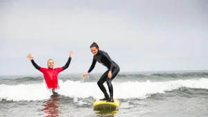 girl surfing on surf board in water with instructor there to help