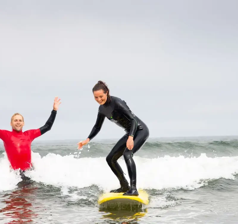 girl surfing on surf board in water with instructor there to help